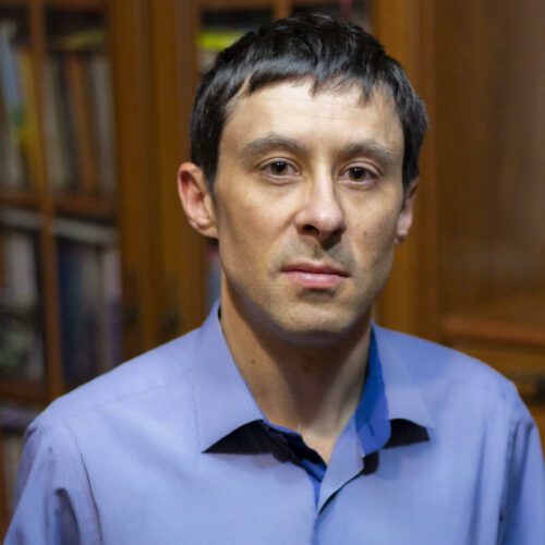 a man in a blue shirt is standing in front of a bookcase.