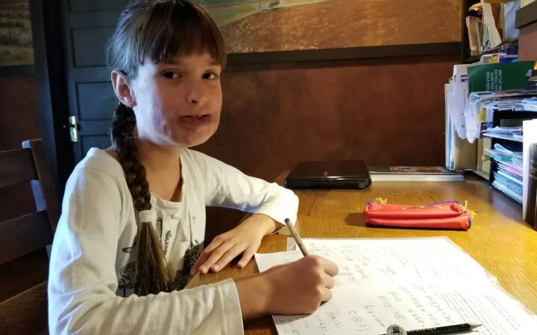 a young girl sitting at a table with a pen and paper.