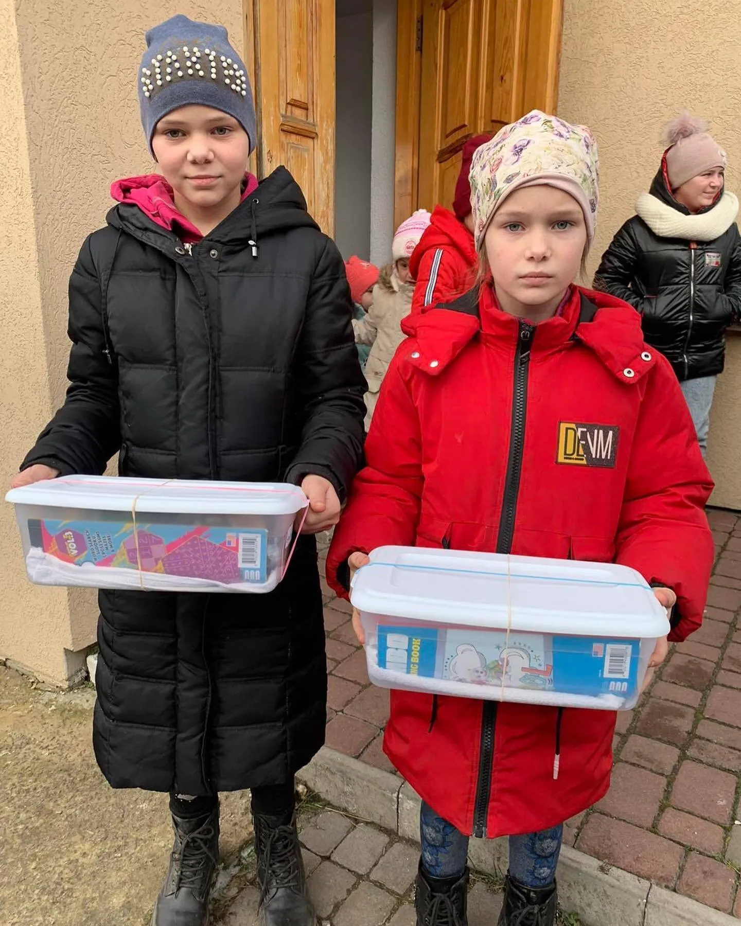 two children holding plastic containers in front of a building.