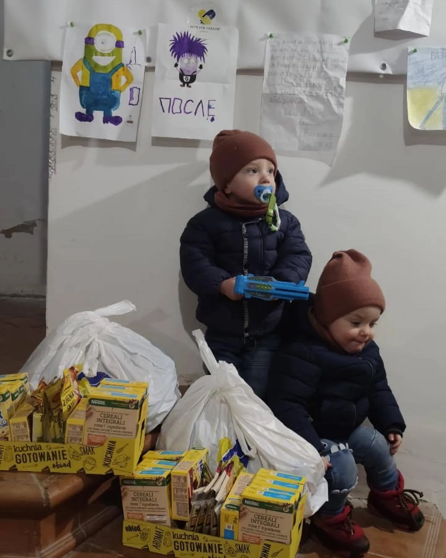 two children sitting on the floor with boxes and bags.