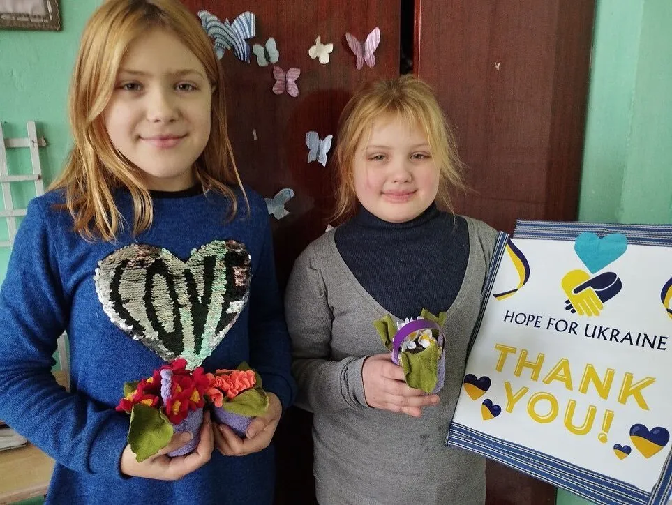 two young girls holding flowers and a thank you sign.