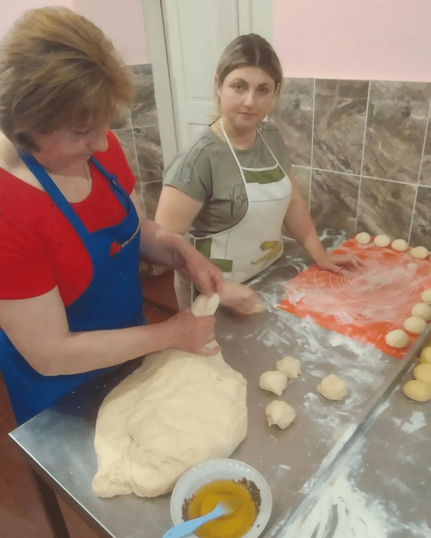 two women in aprons making dough on a table.