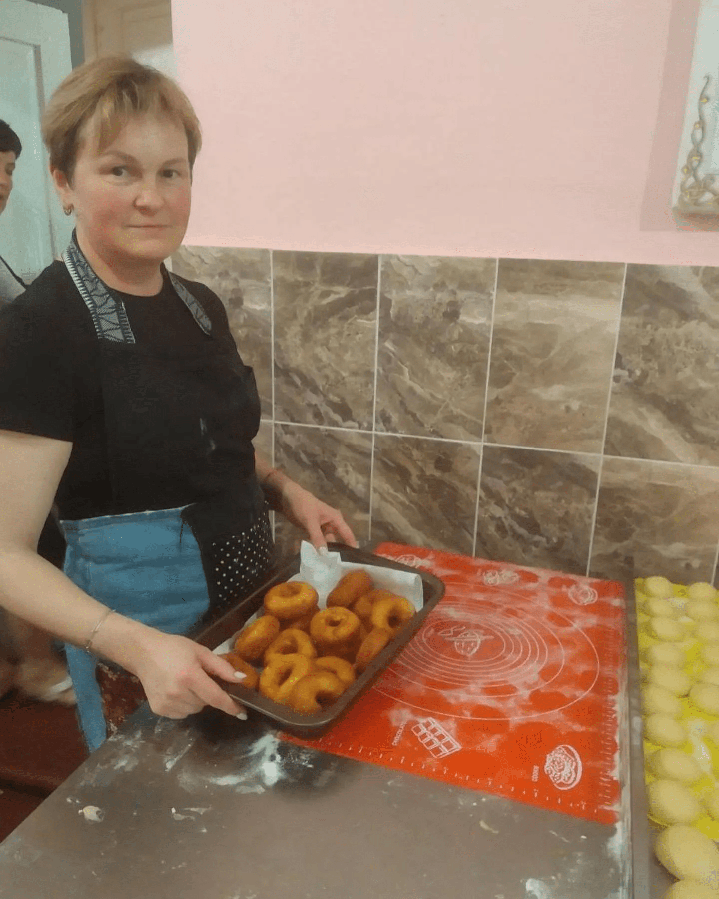 a woman holding a tray of doughnuts in a kitchen.