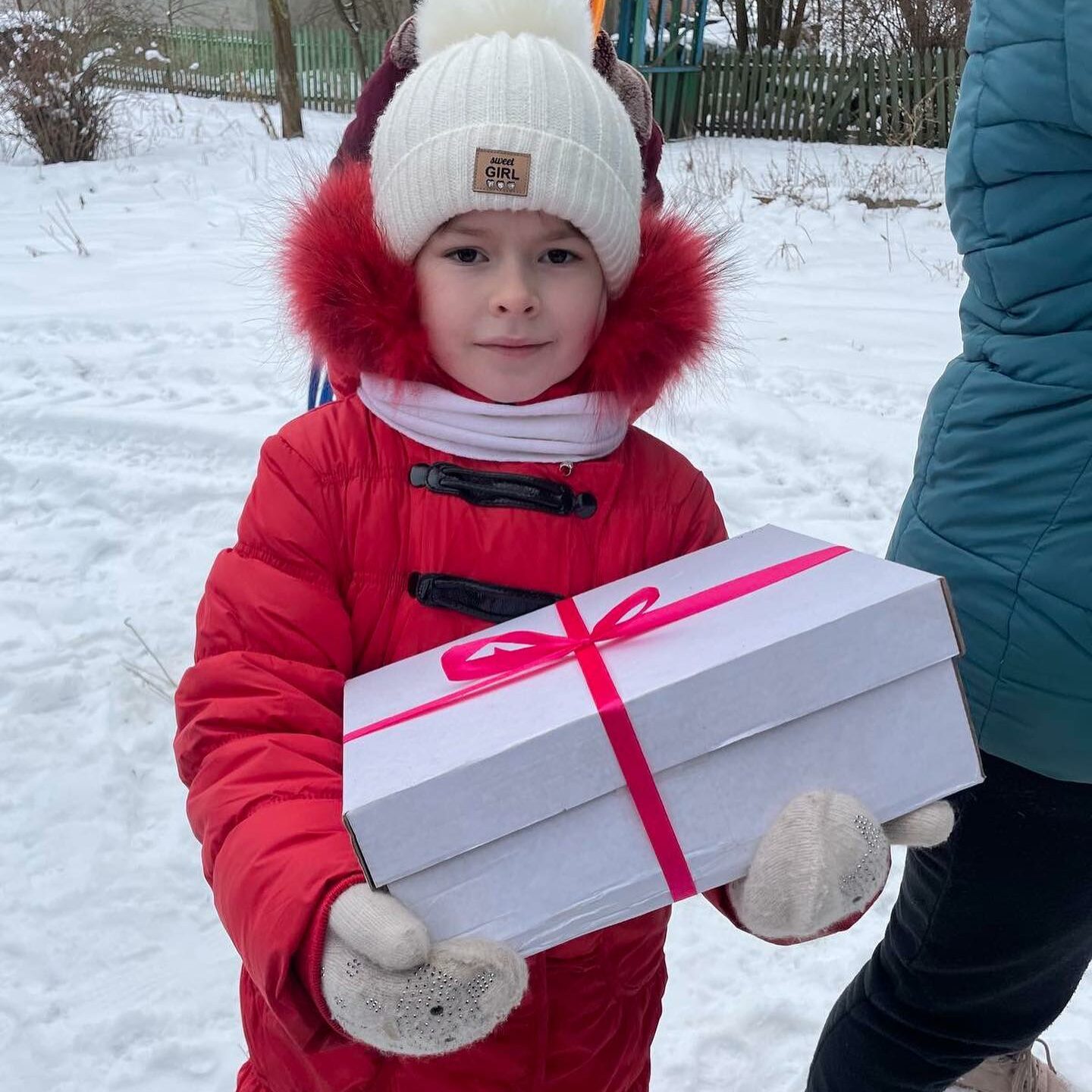 a small child in a red coat holding a white box.