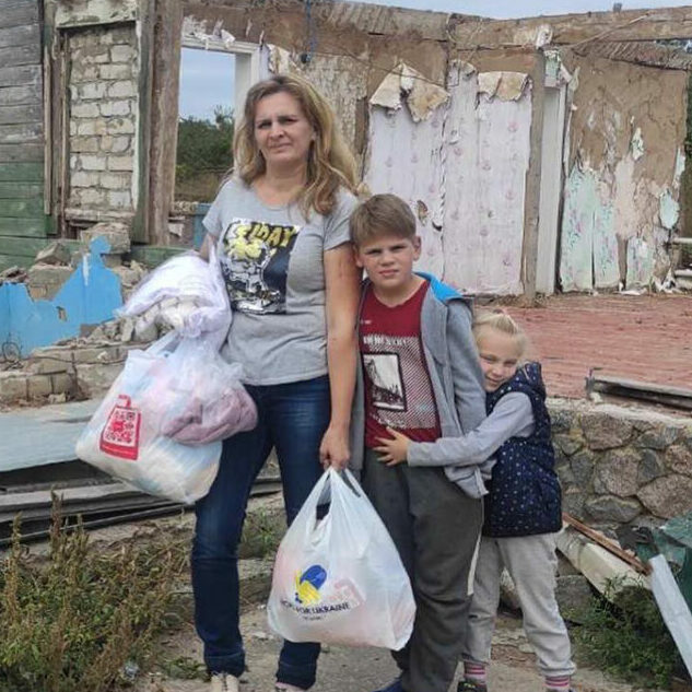 a woman and two children standing in front of a destroyed building.