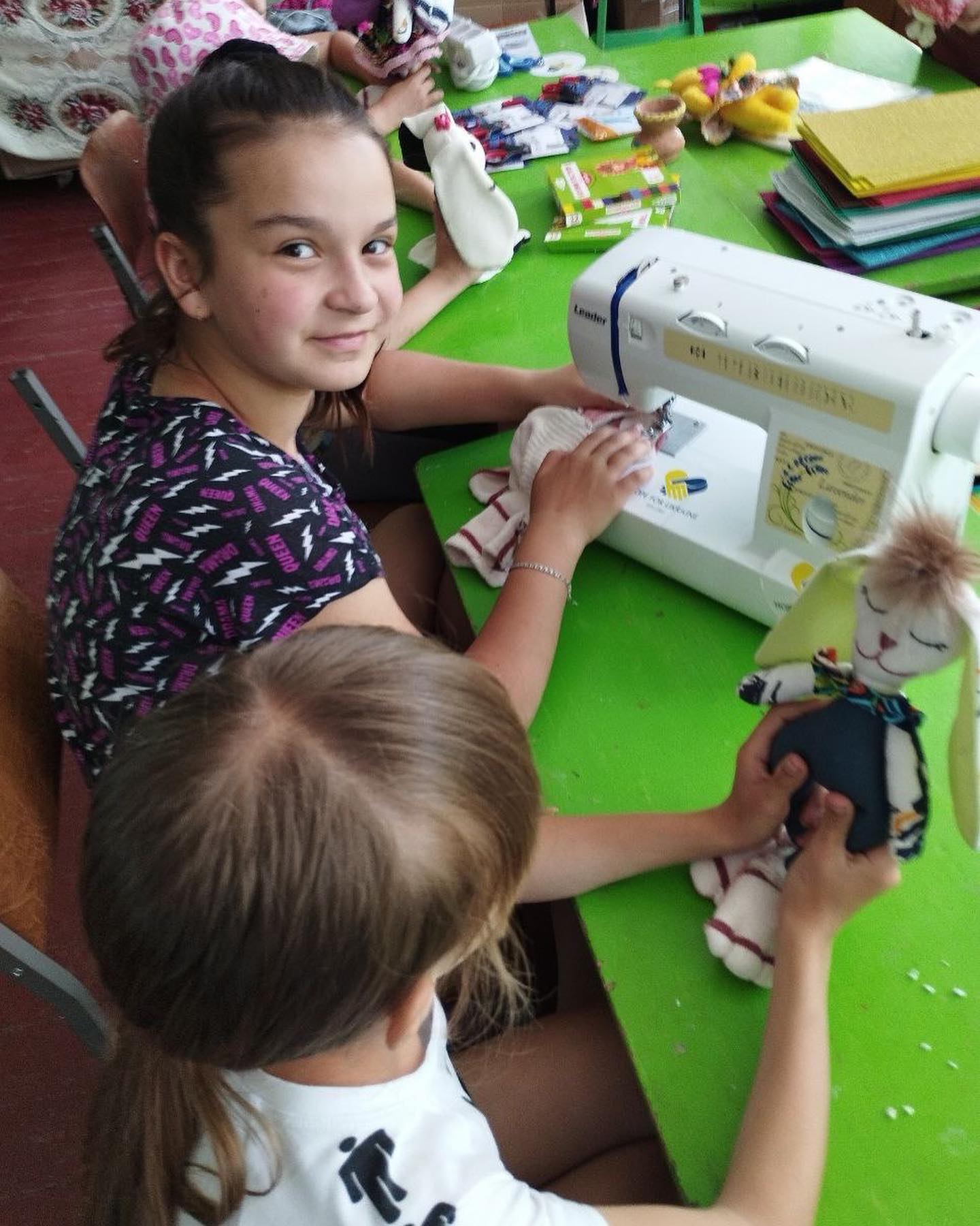 a girl and a girl sitting at a table with a sewing machine.