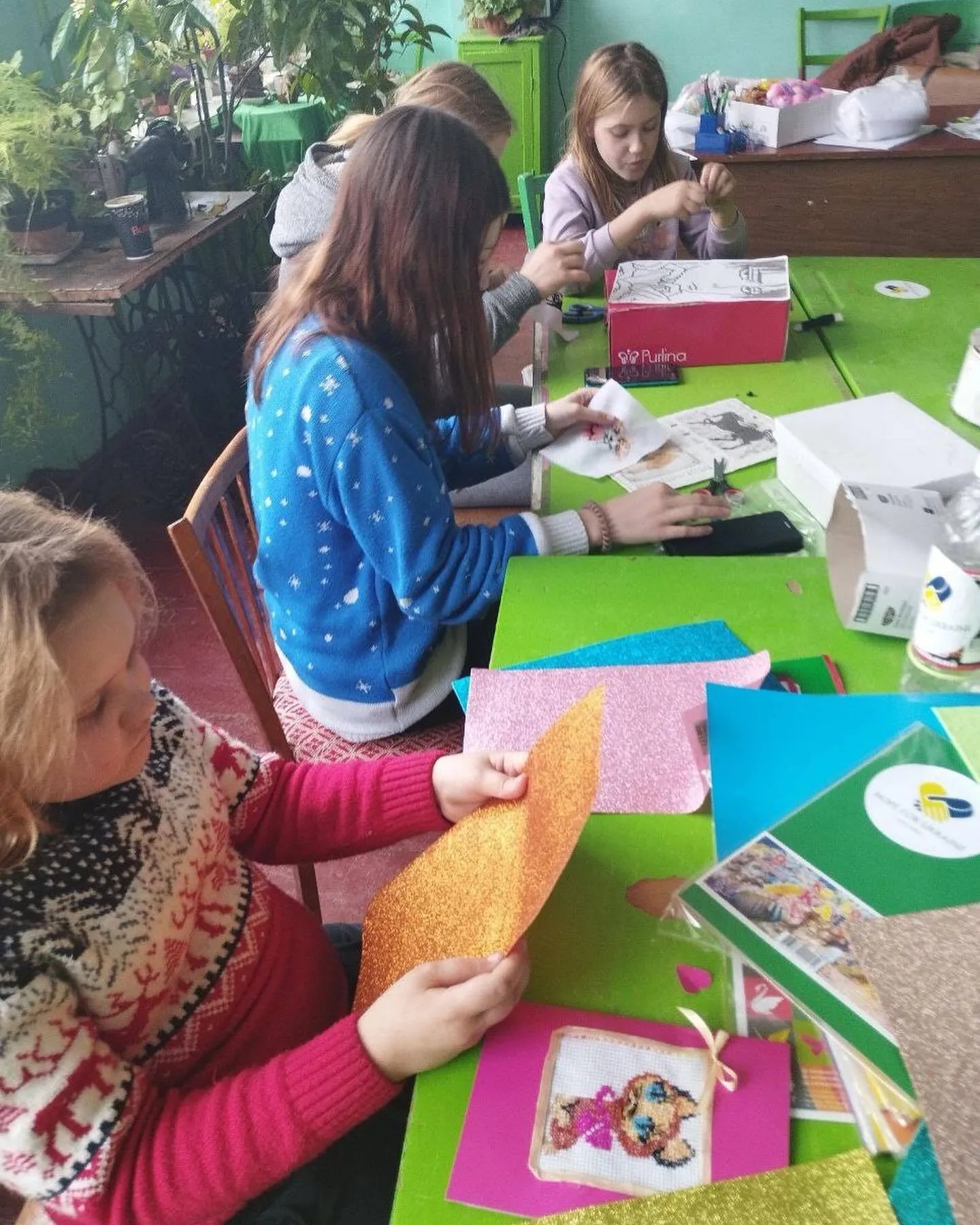 a group of girls sitting at a table working on crafts.