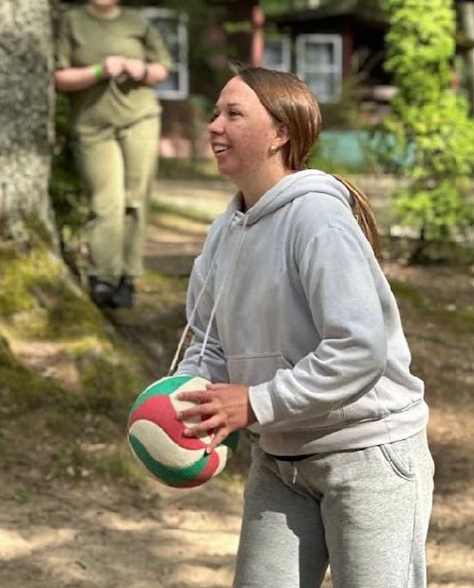 a girl is holding a volleyball ball in the woods.