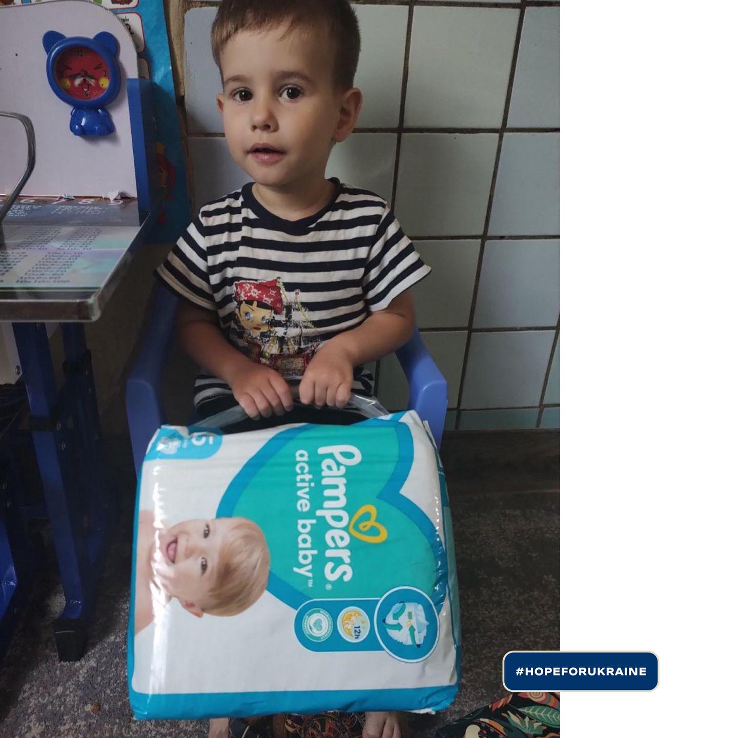 a young boy sitting in a chair holding a pack of pampers diapers.