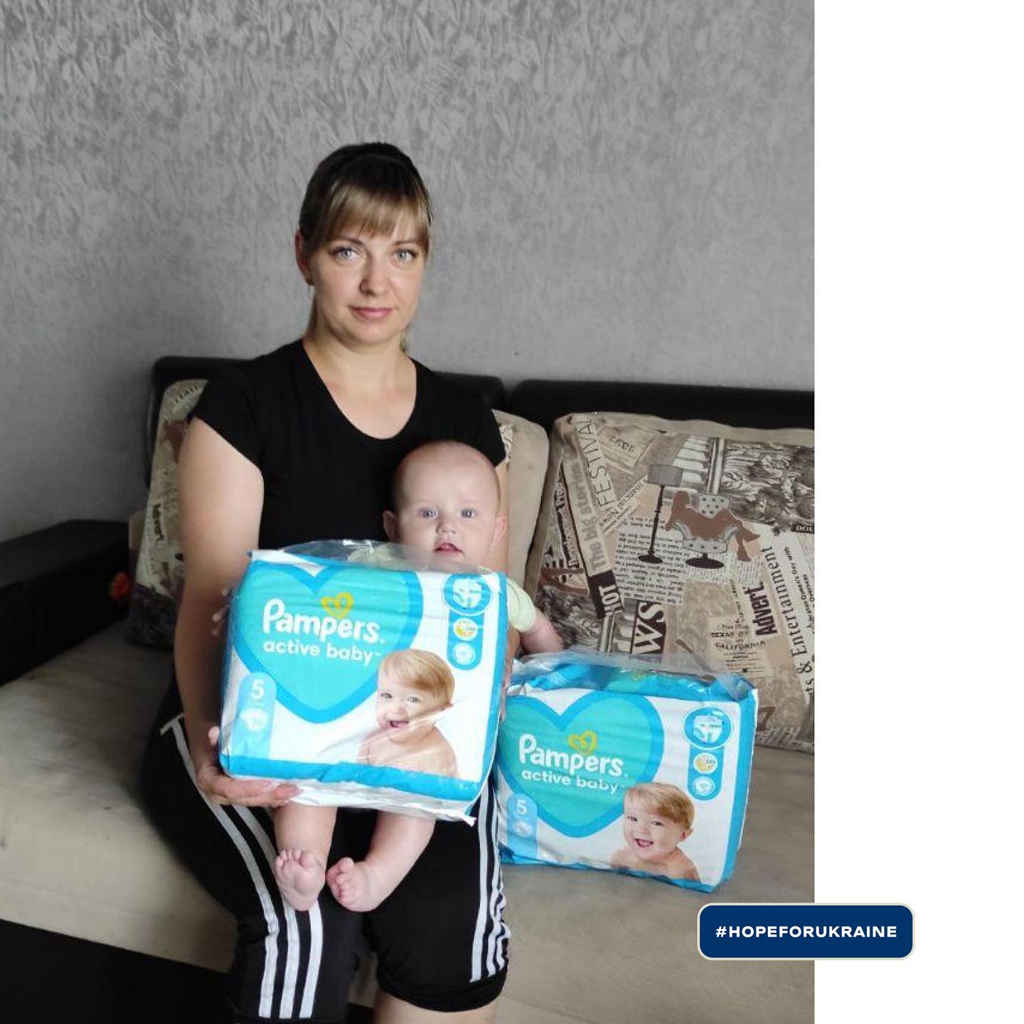 a woman with a baby sitting on a couch holding a pack of pampers diapers.