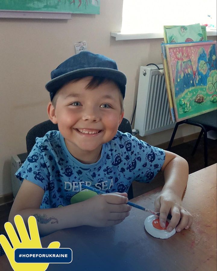 a young boy smiles at a table while painting.