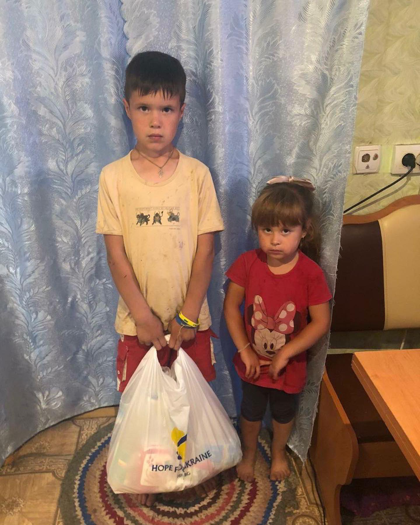 two children standing next to each other holding bags.
