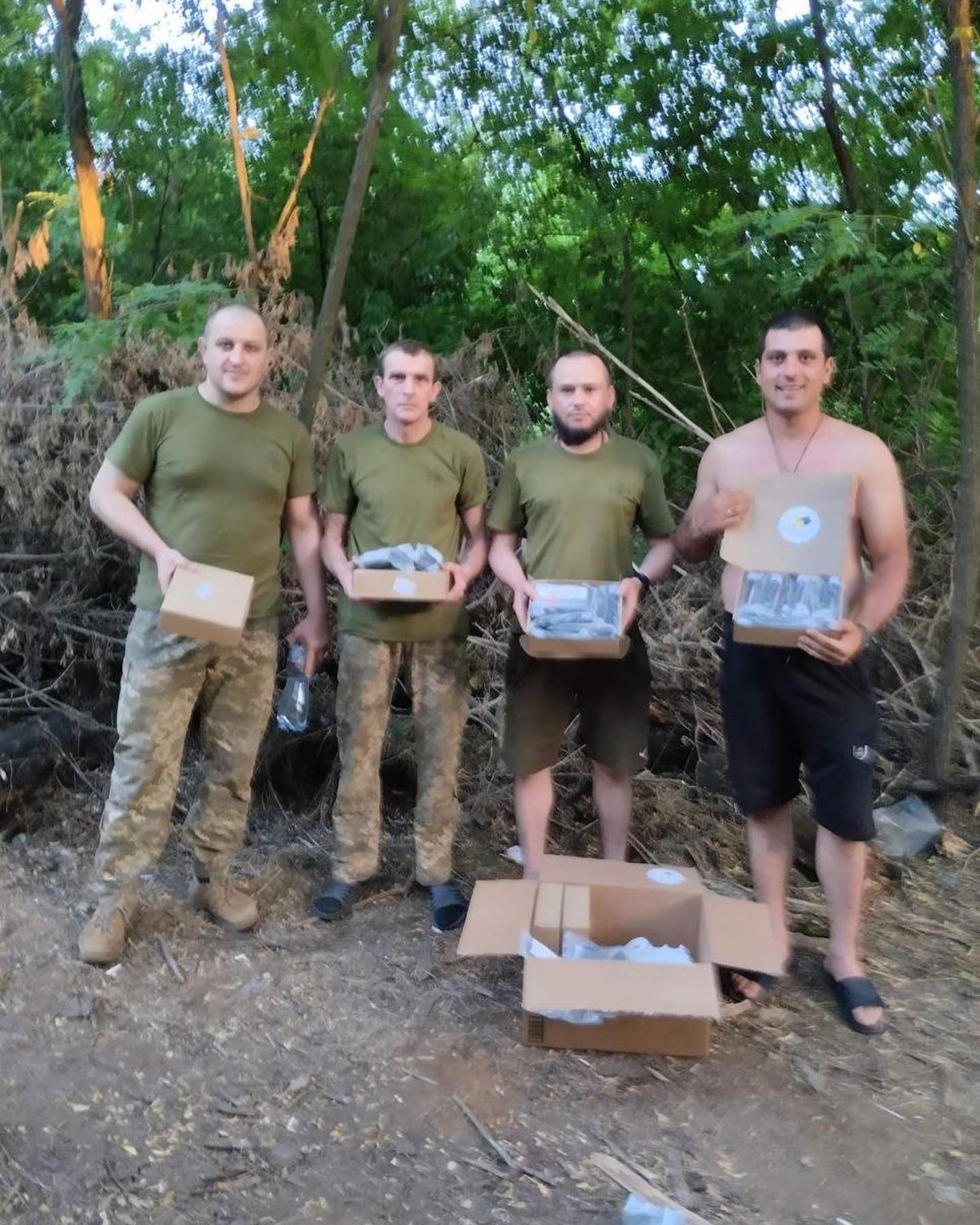 a group of men standing in a wooded area holding boxes.