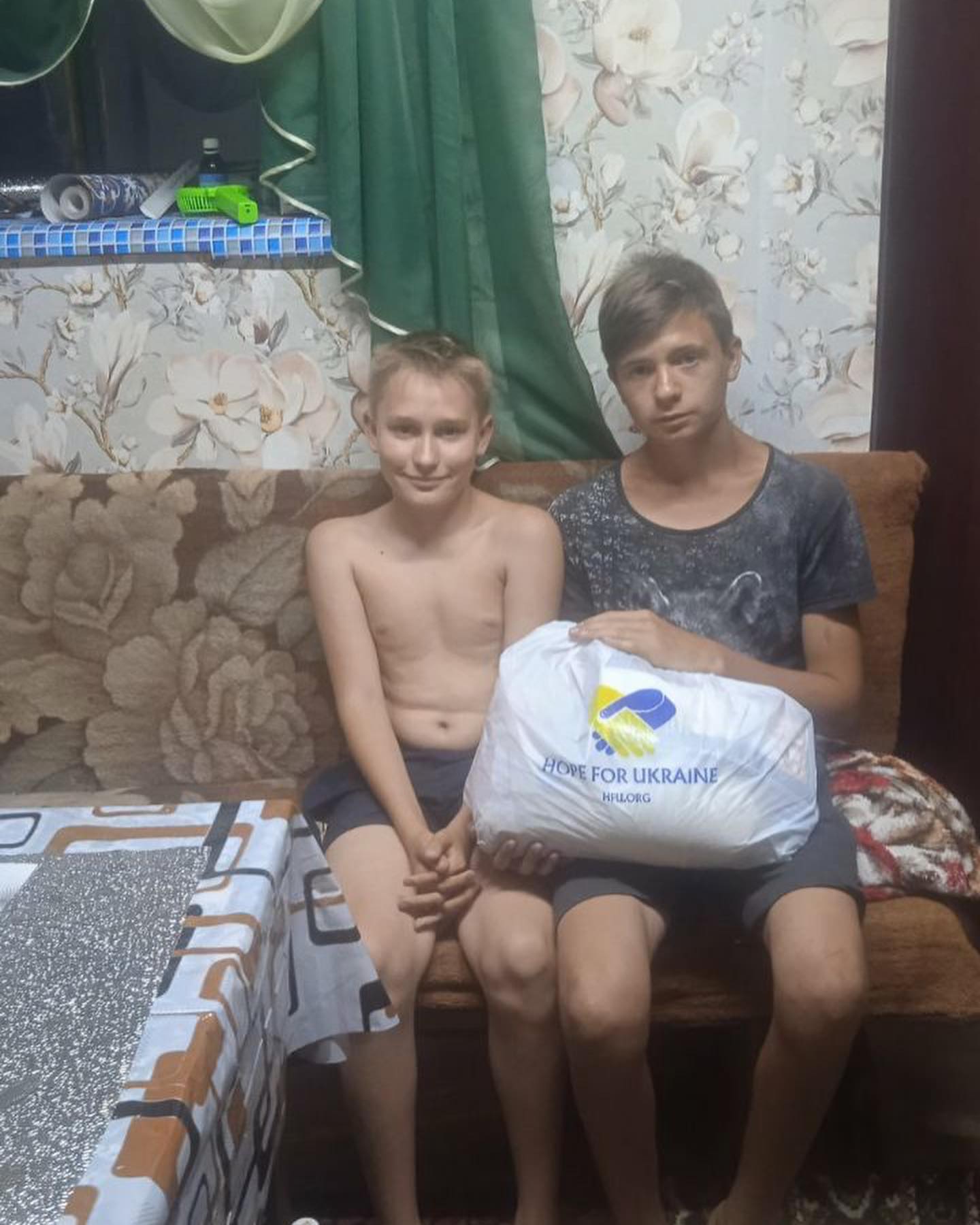 two boys sitting on a couch with a bag.