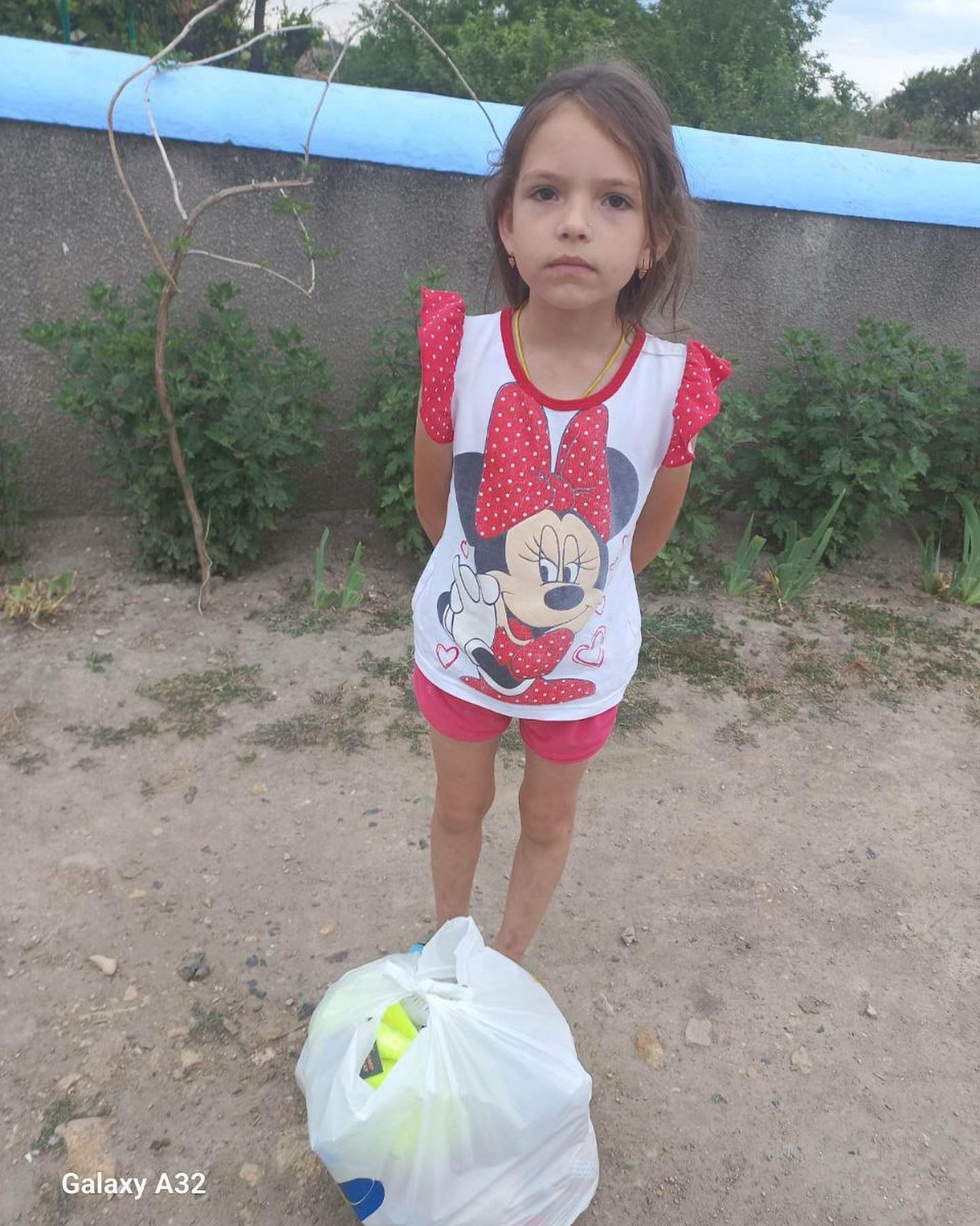 a little girl standing next to a garbage bag.