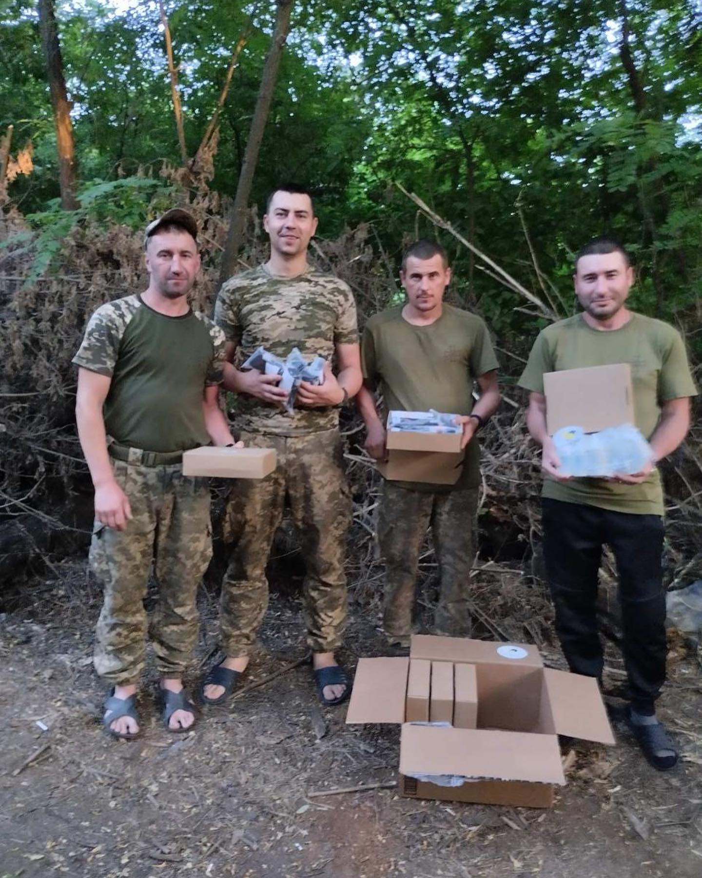 a group of men standing next to boxes in the woods.