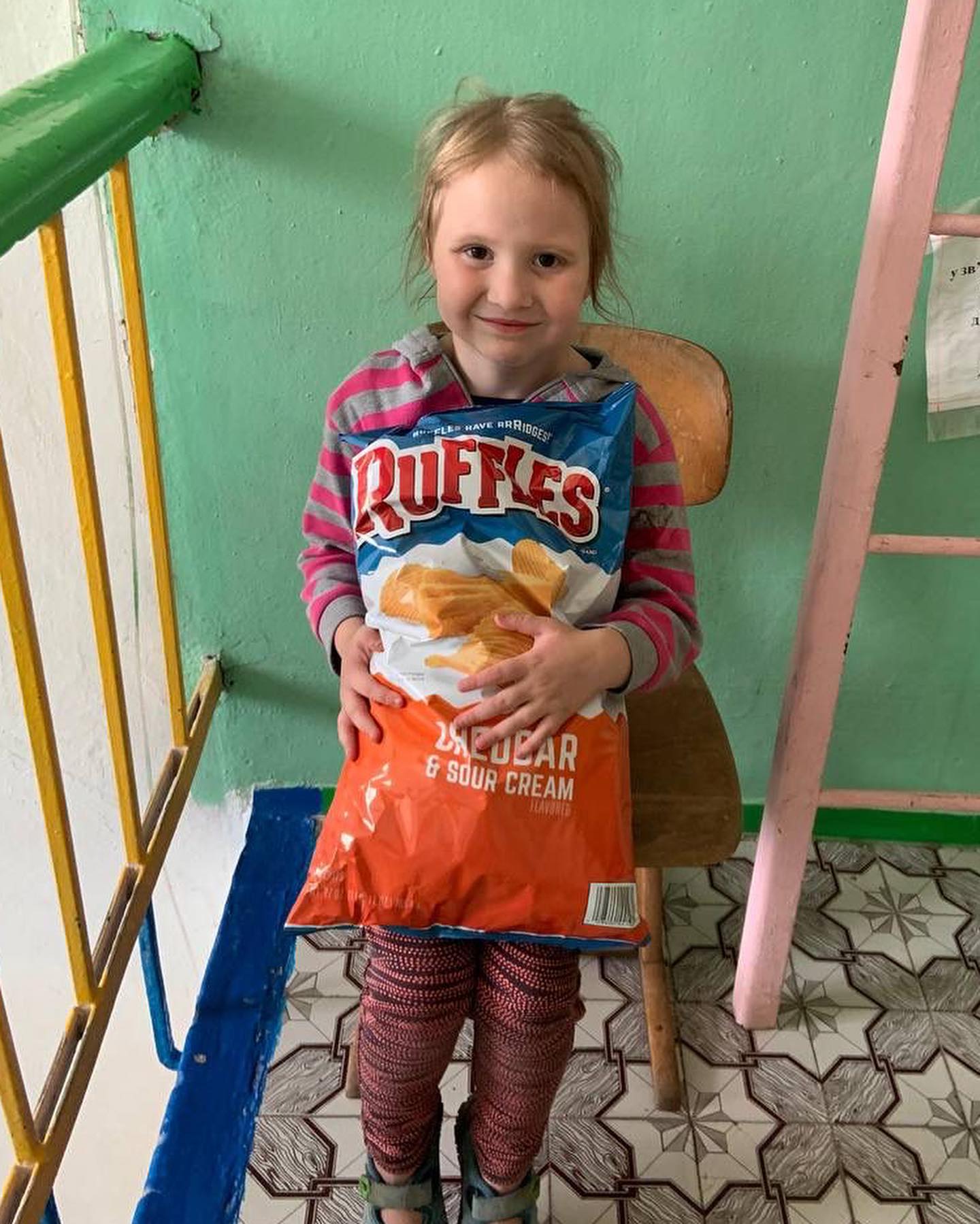 a little girl sitting on a chair holding a bag of doritos.