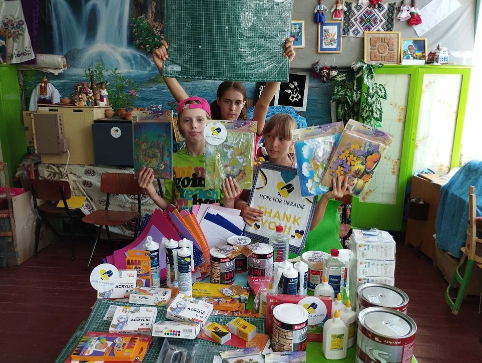 A group of children posing in front of a table full of art supplies.