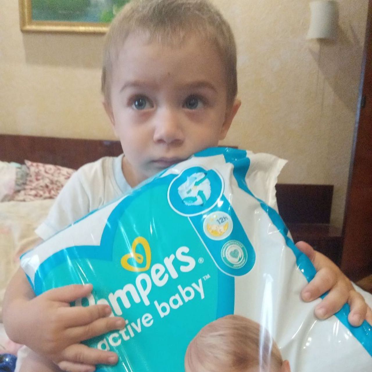 A little boy holding up a pack of pampers natural baby diapers.