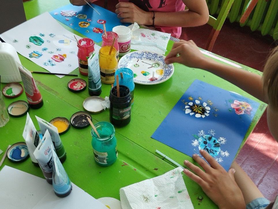 A group of children are painting on a green table.