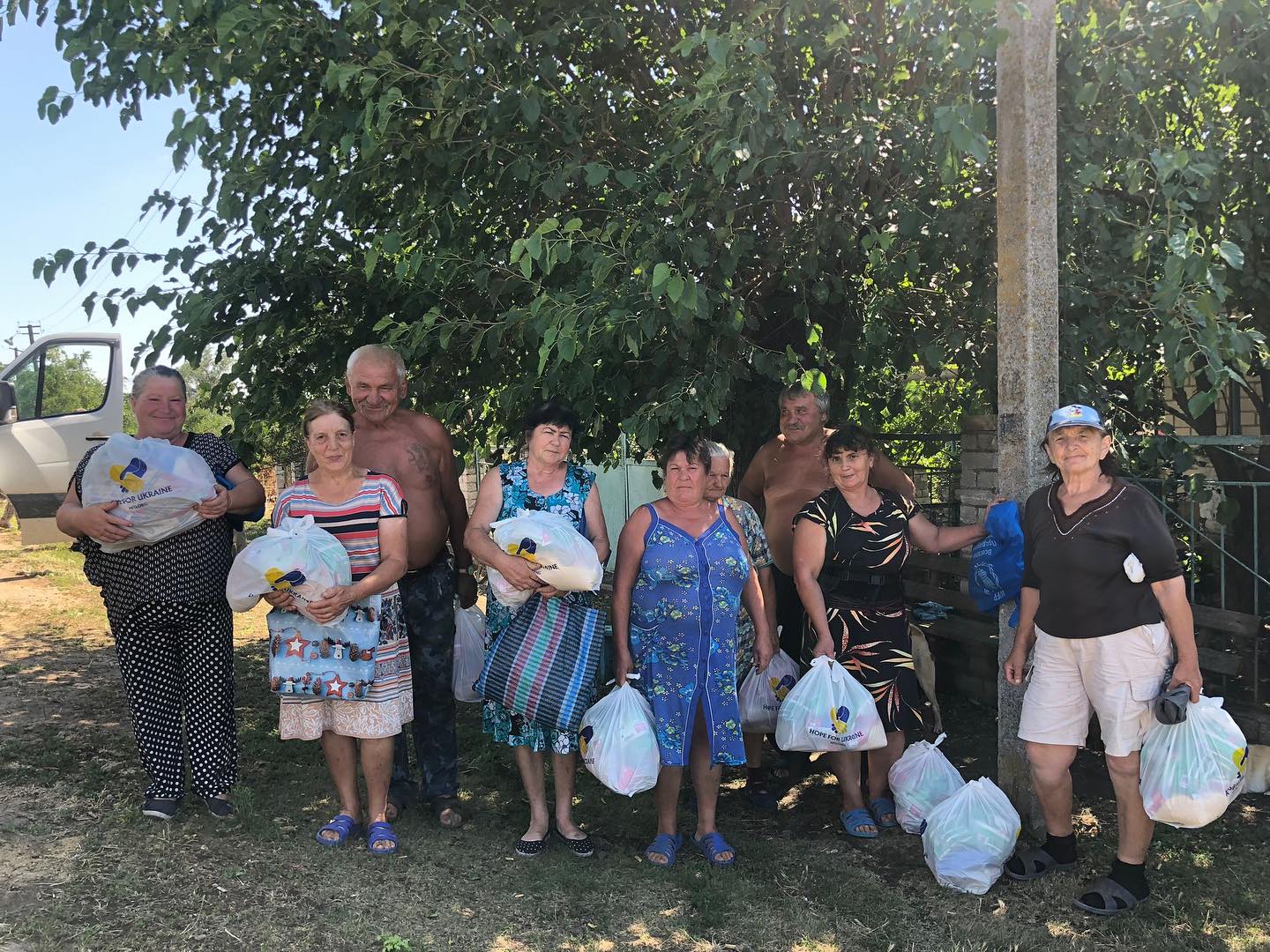A group of people standing in front of a tree with bags.