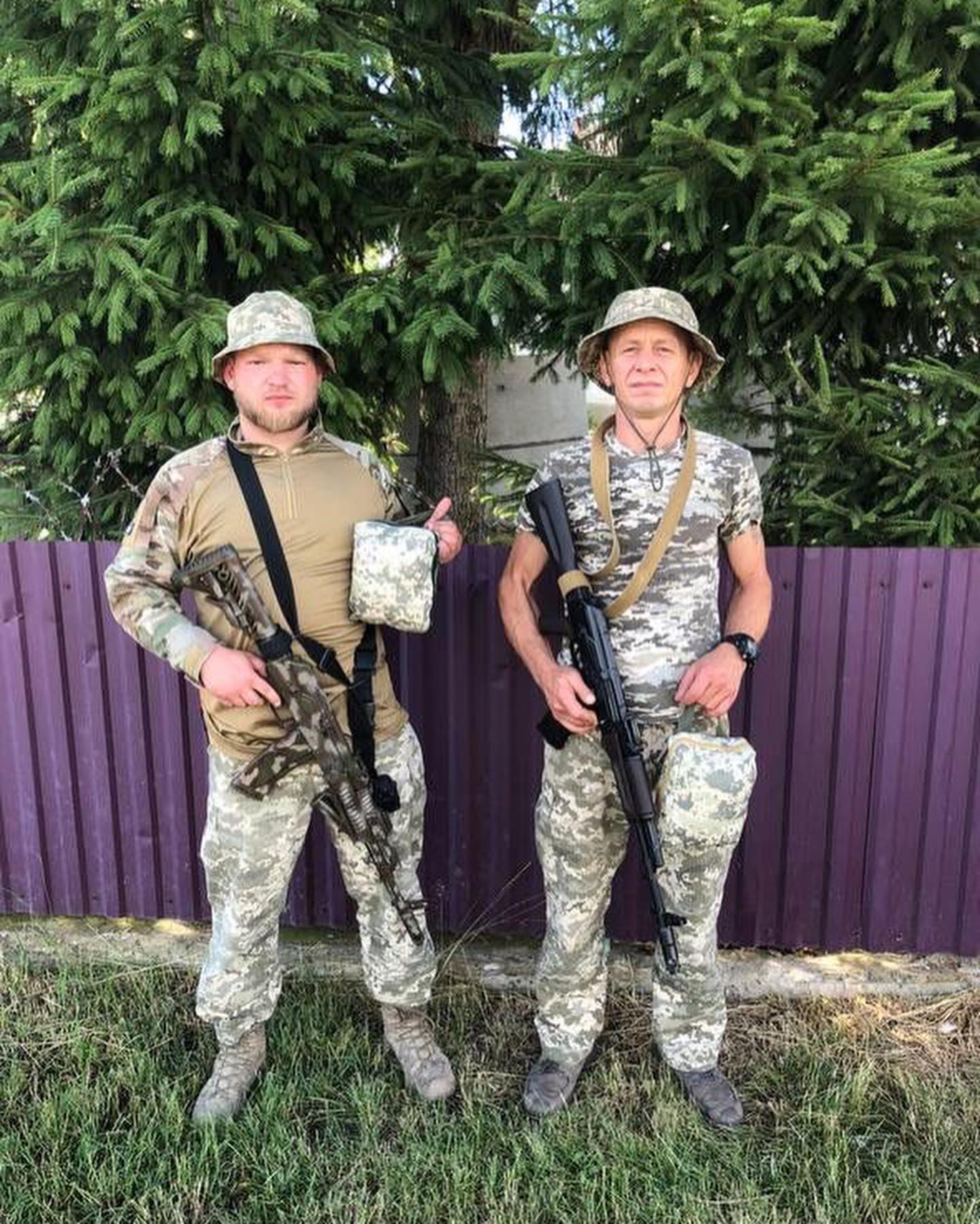Two men in camouflage standing next to a fence.