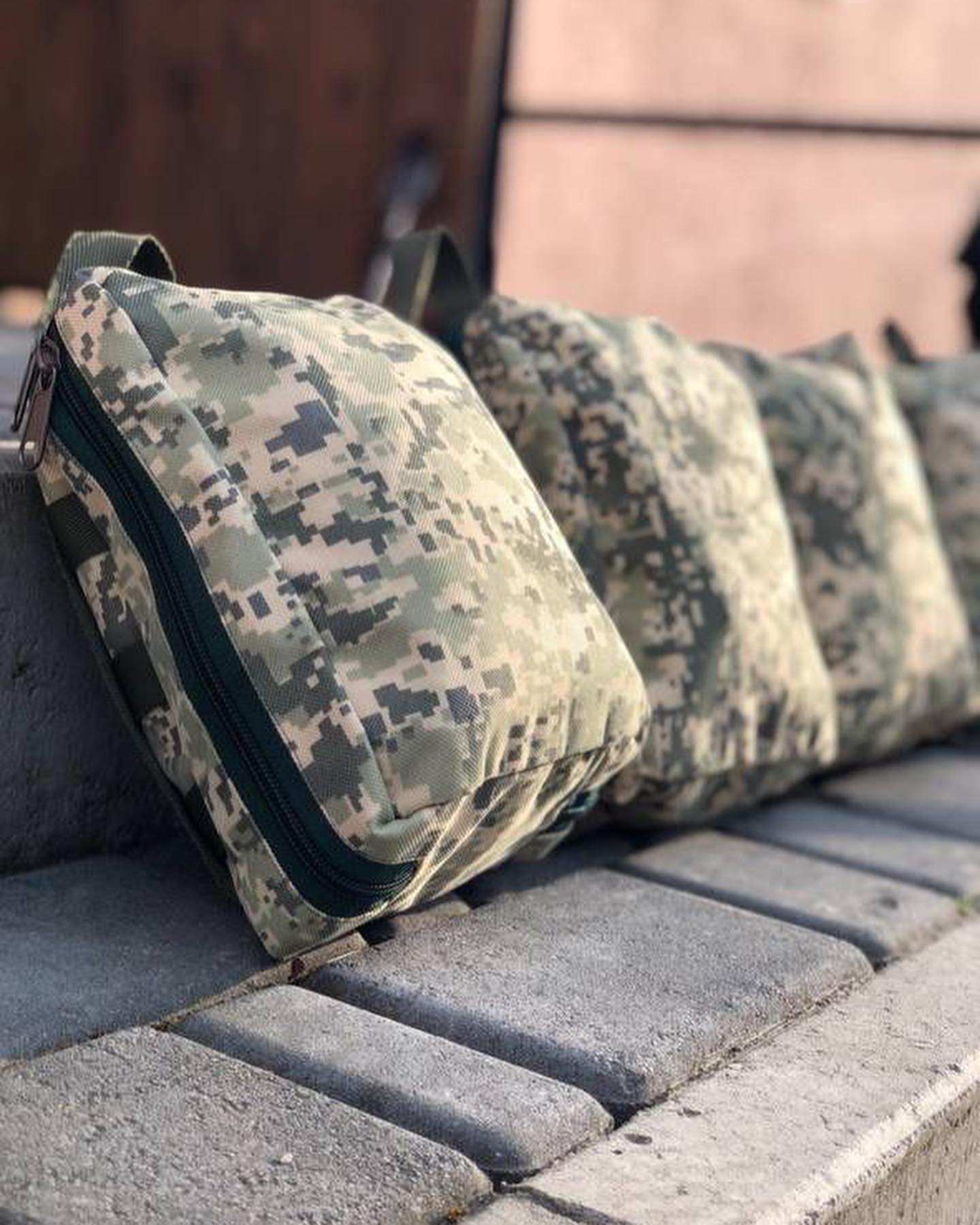 Four camouflage bags sitting on a bench.