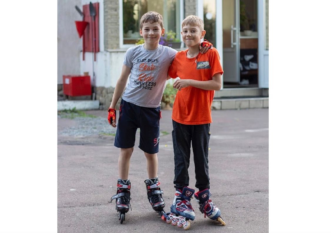 Two boys standing next to each other on roller skates.