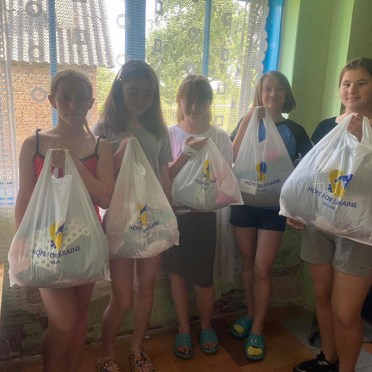 A group of girls holding shopping bags in front of a window.