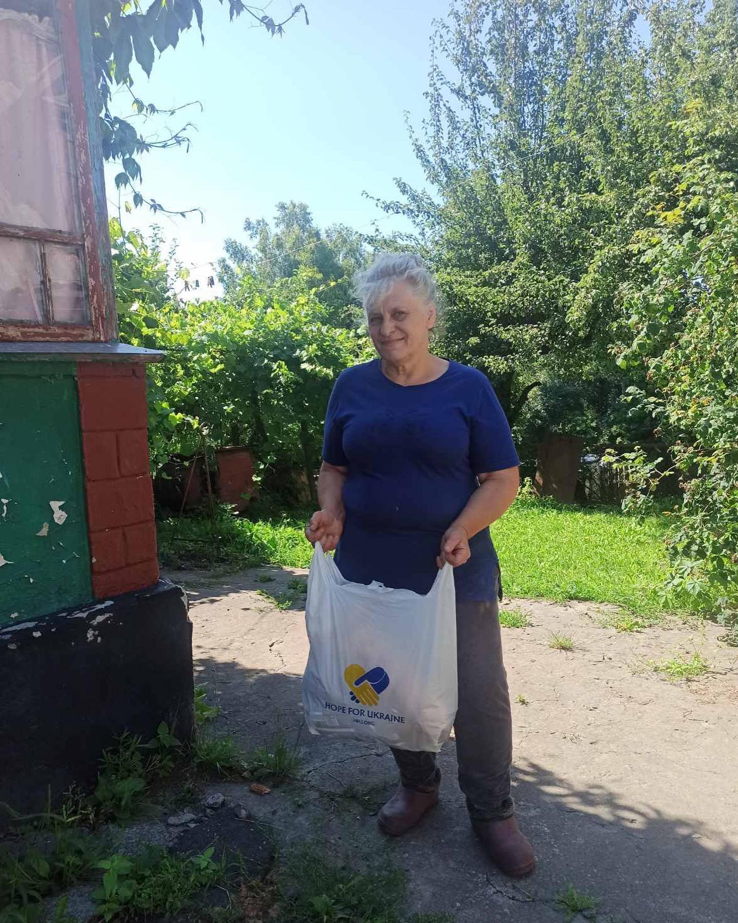 A woman holding a shopping bag in front of a house.