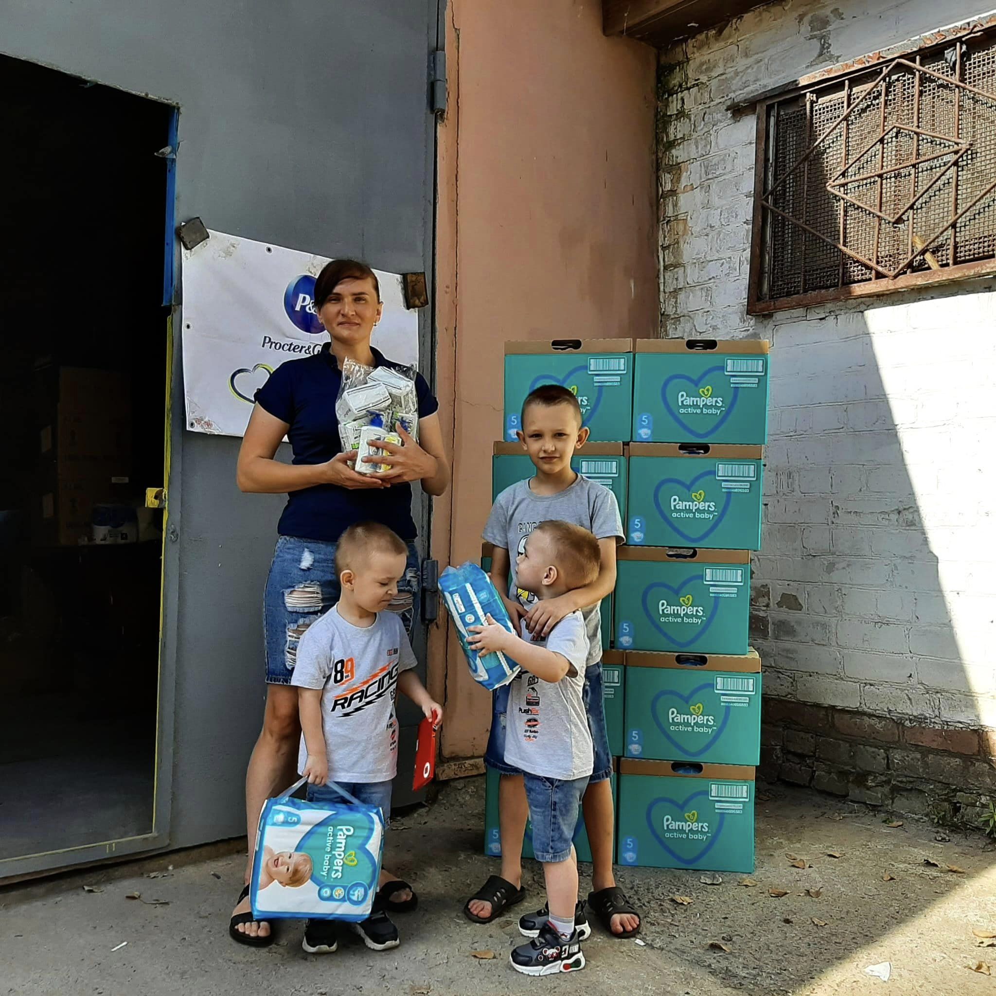 A woman and two children standing in front of boxes of diapers.