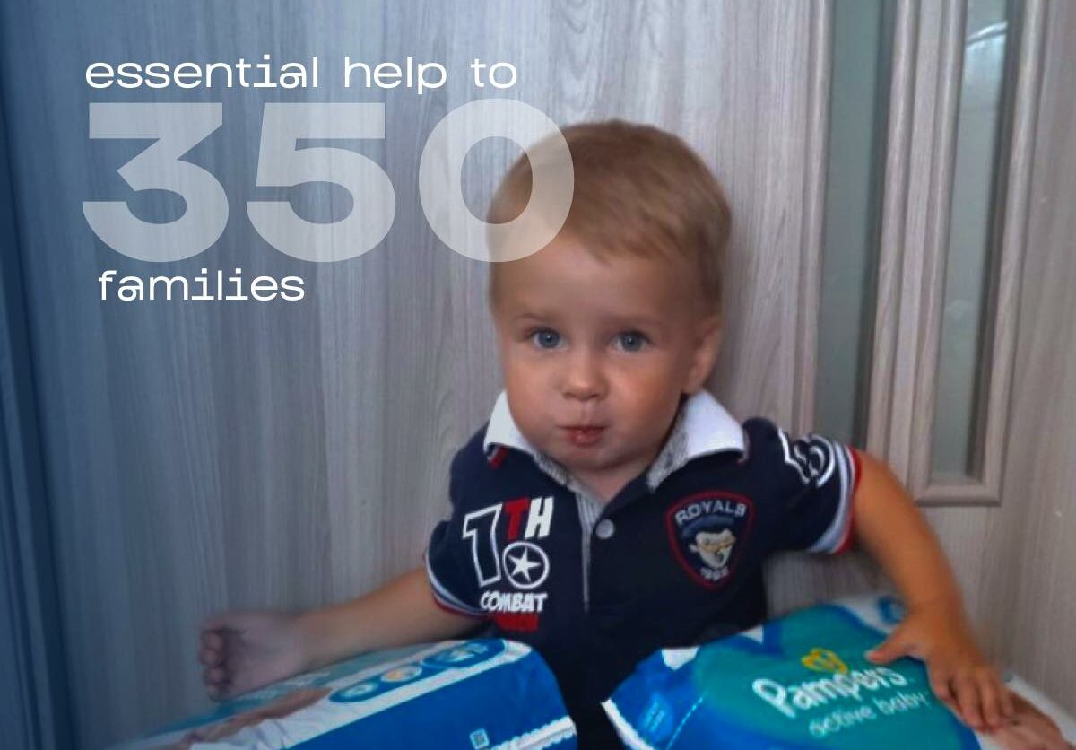 A young boy holding a pack of diapers with the words essential help to 350 families.