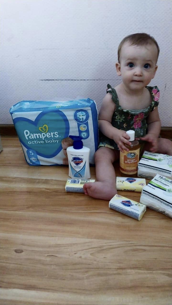 A baby sits on the floor next to a box of diapers.