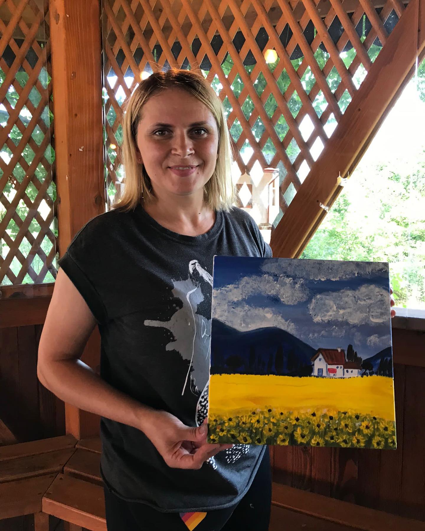 A woman holding up a painting of a sunflower field.