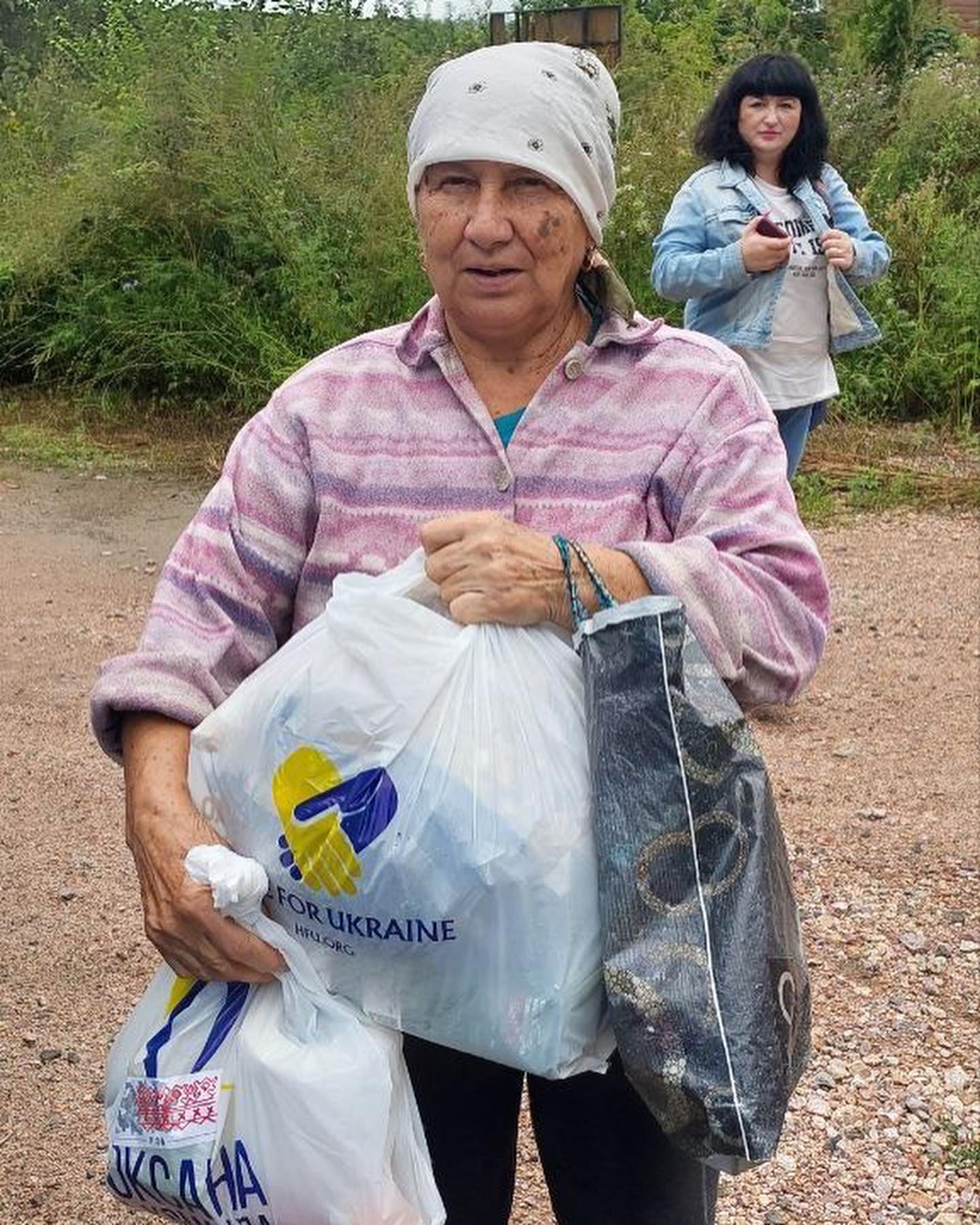A woman carrying bags of food on a dirt road.
