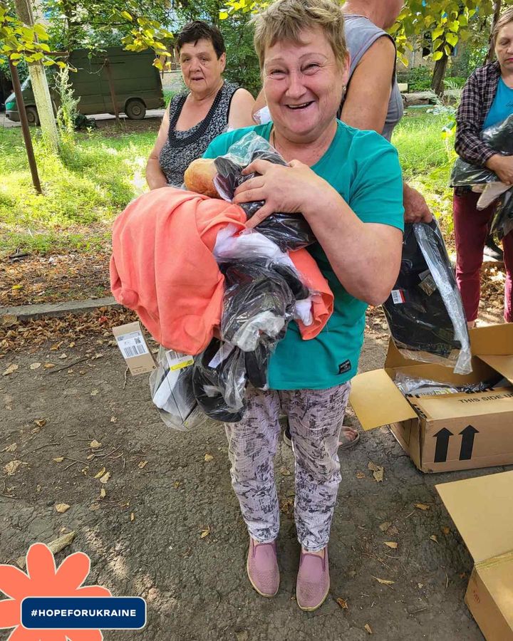A woman holding a box of clothes in a park.