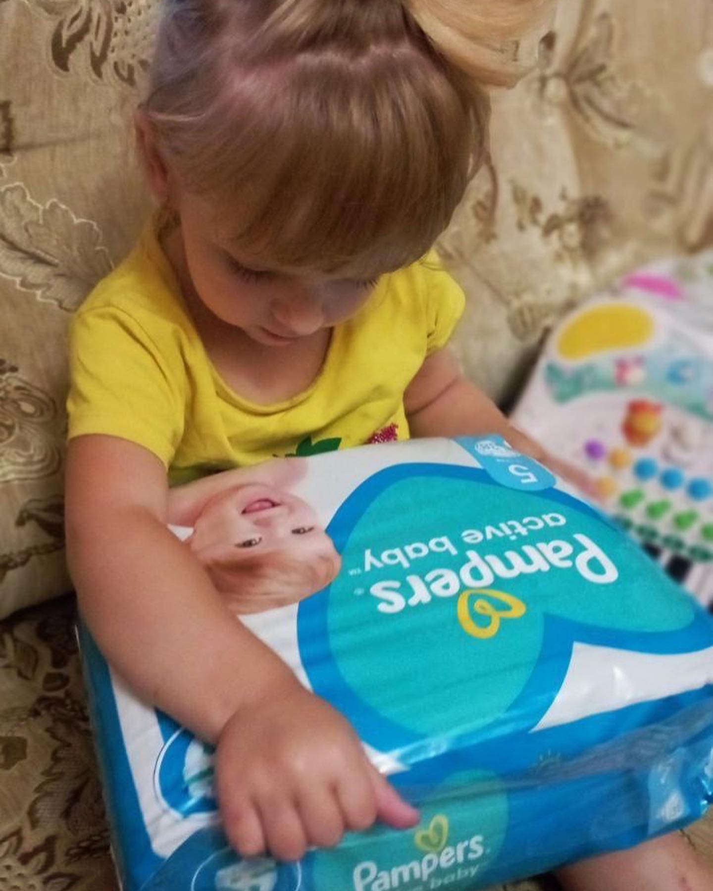 A little girl playing with a pack of pampers diapers.