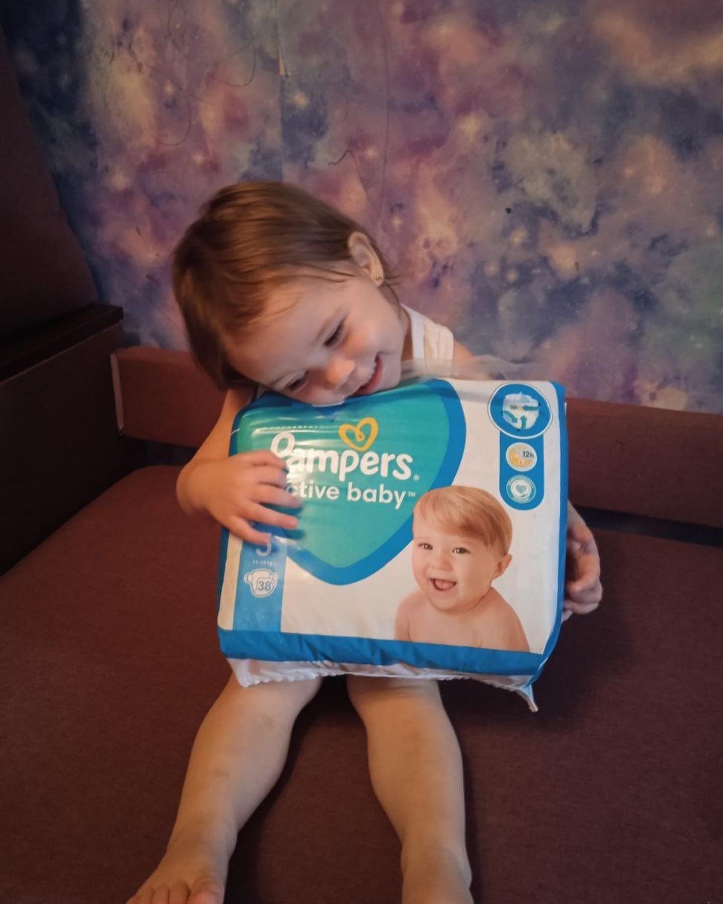 A little girl is holding a pack of pampers diapers.