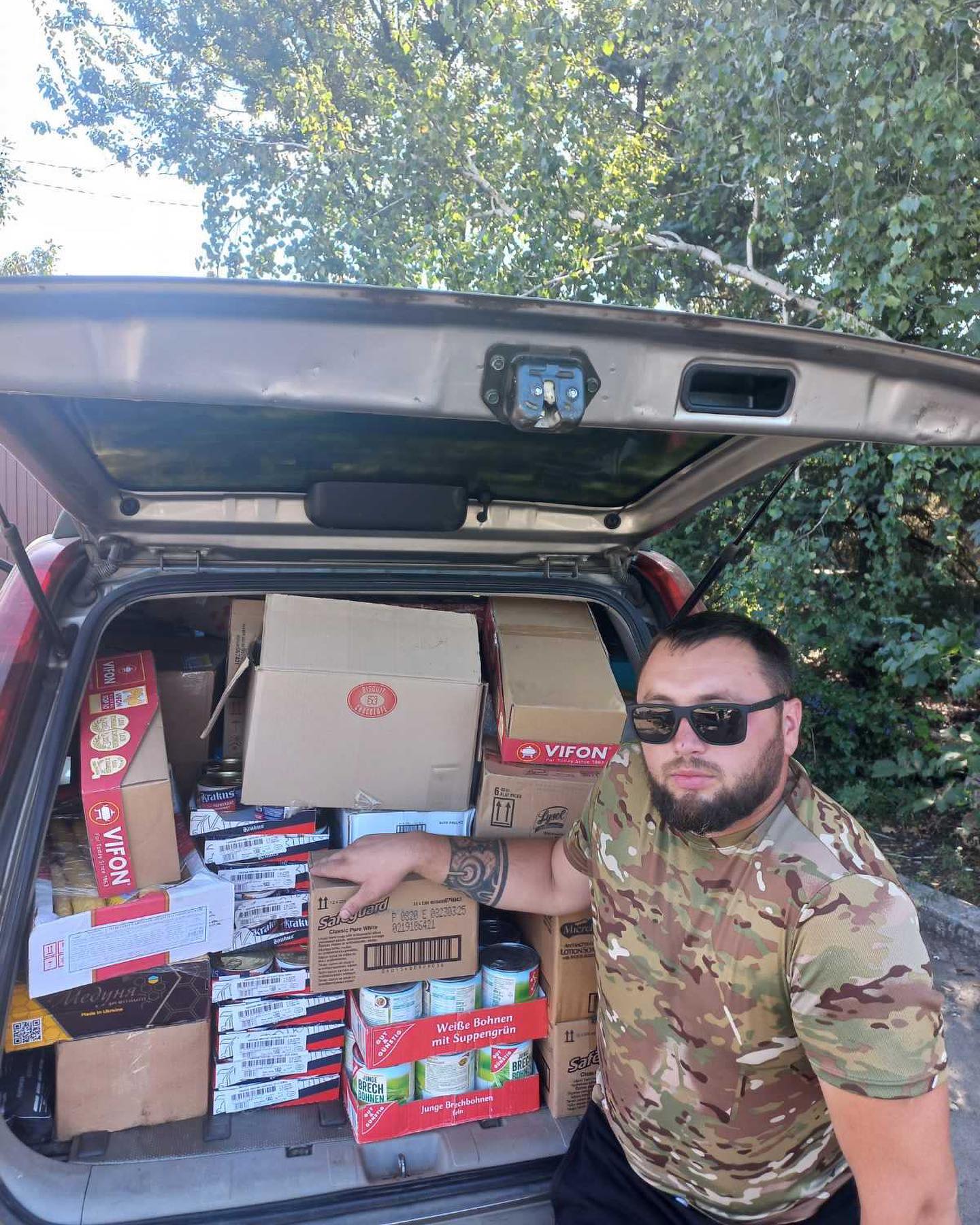 A man standing in the trunk of a car with boxes of food.