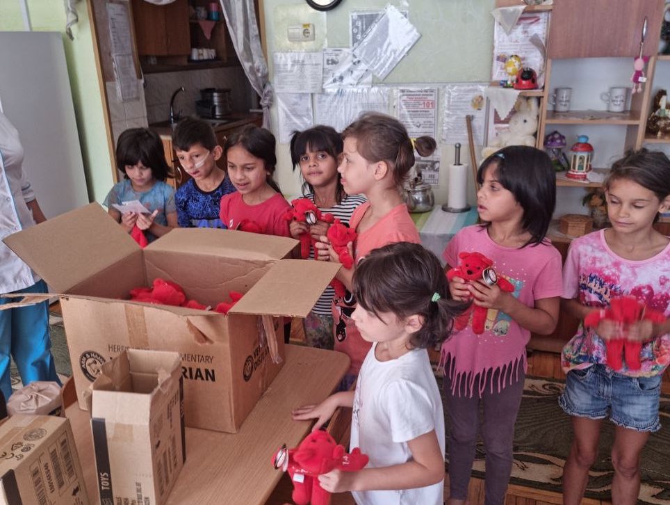 A group of children are standing around a box of stuffed animals.