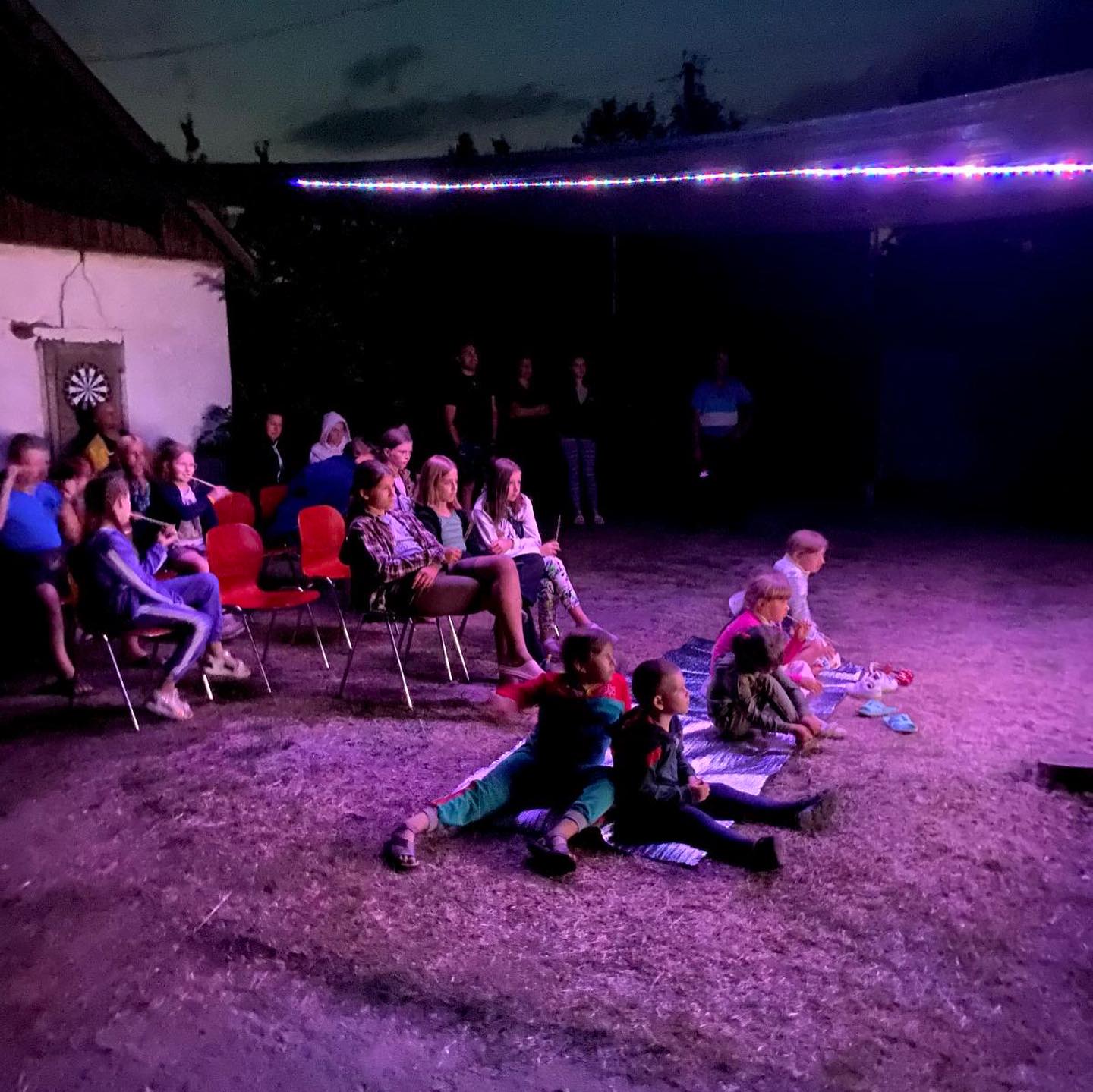 A group of people sitting on chairs in a field at night.