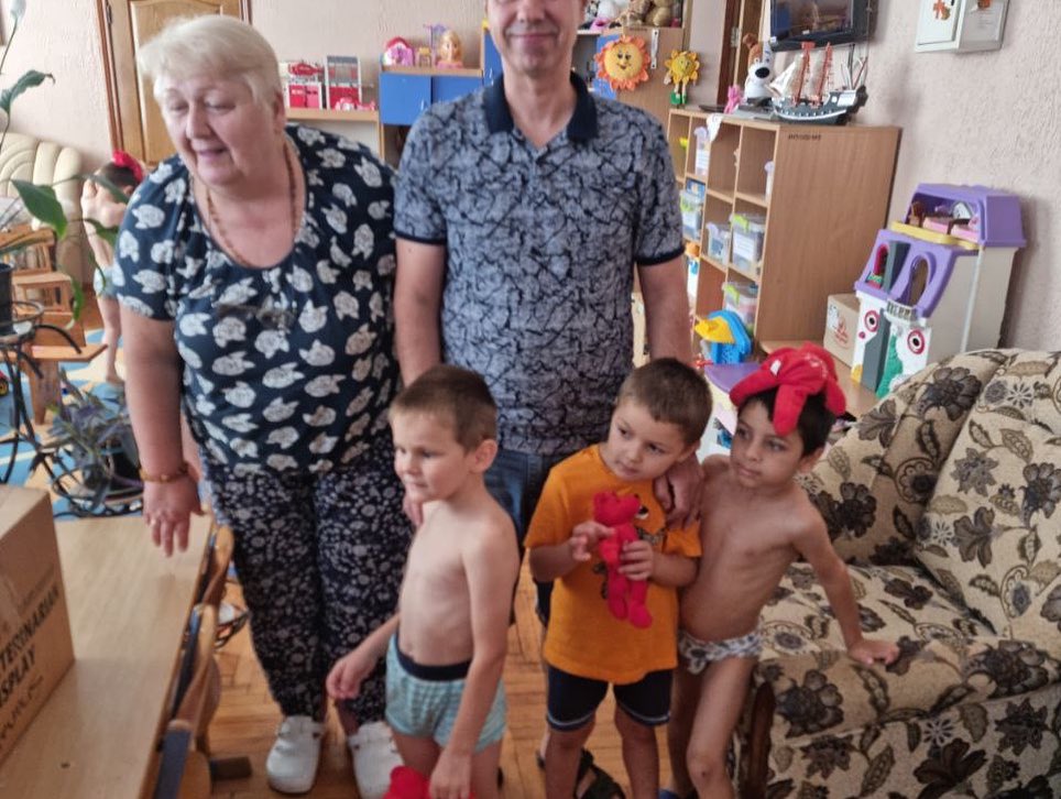 A group of people standing in a living room with children.