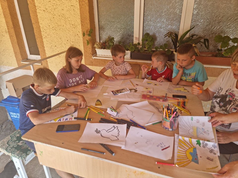 A group of children are sitting around a table with paper and crayons.
