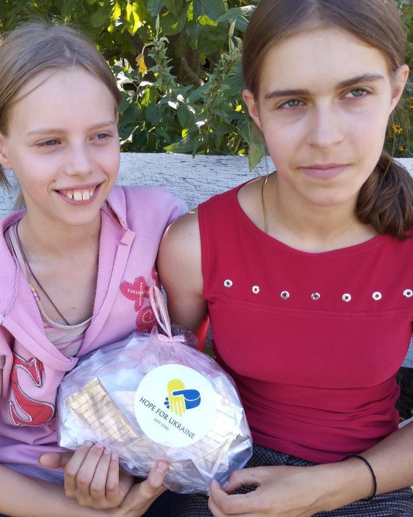 Two girls sitting on a bench holding a bag of cookies.