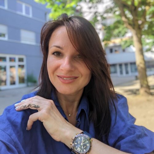 A woman wearing a blue shirt and a watch in front of a building.