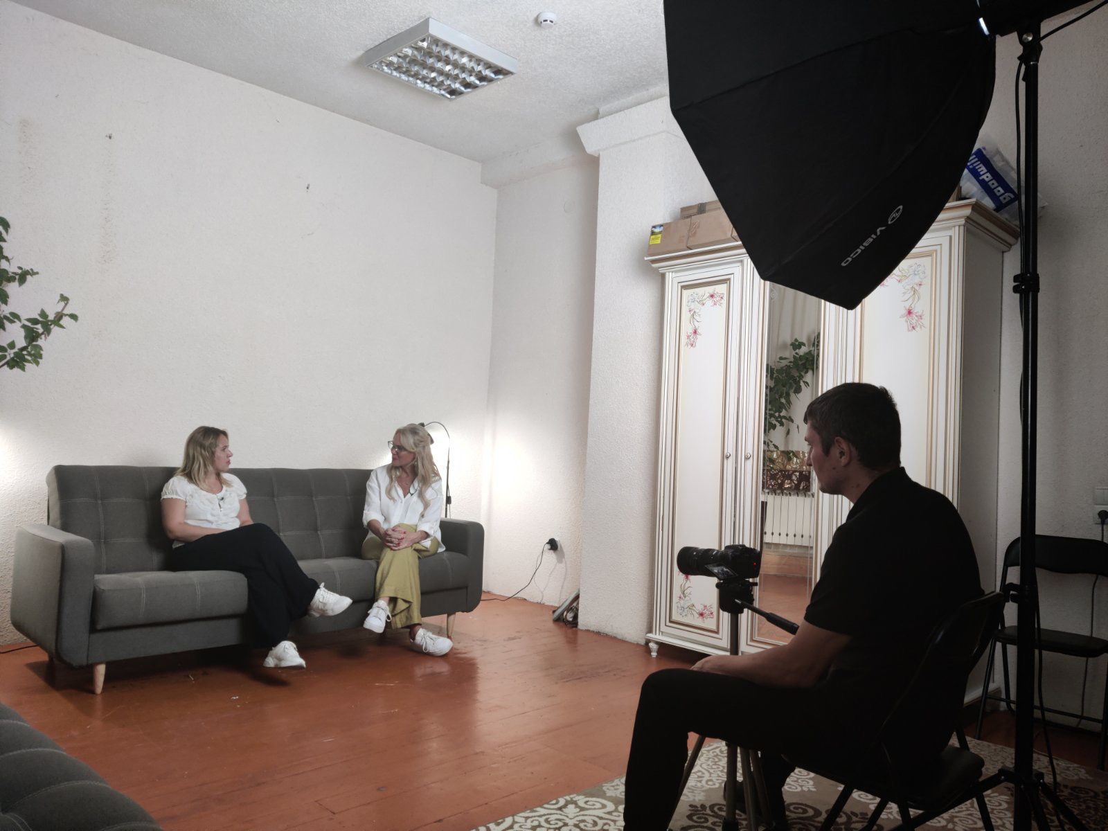 Two people sitting on a couch in a room with a camera.