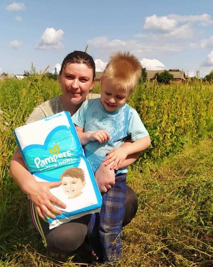 A woman and a child in a field holding a pack of diapers.