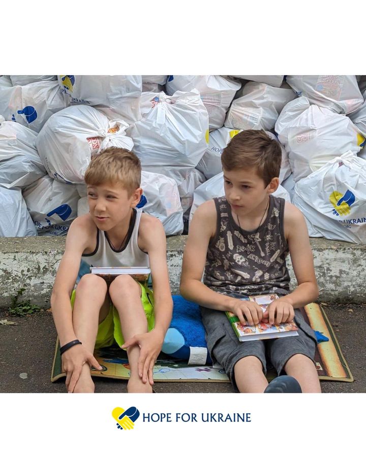 Two boys sitting on the ground next to a pile of bags.