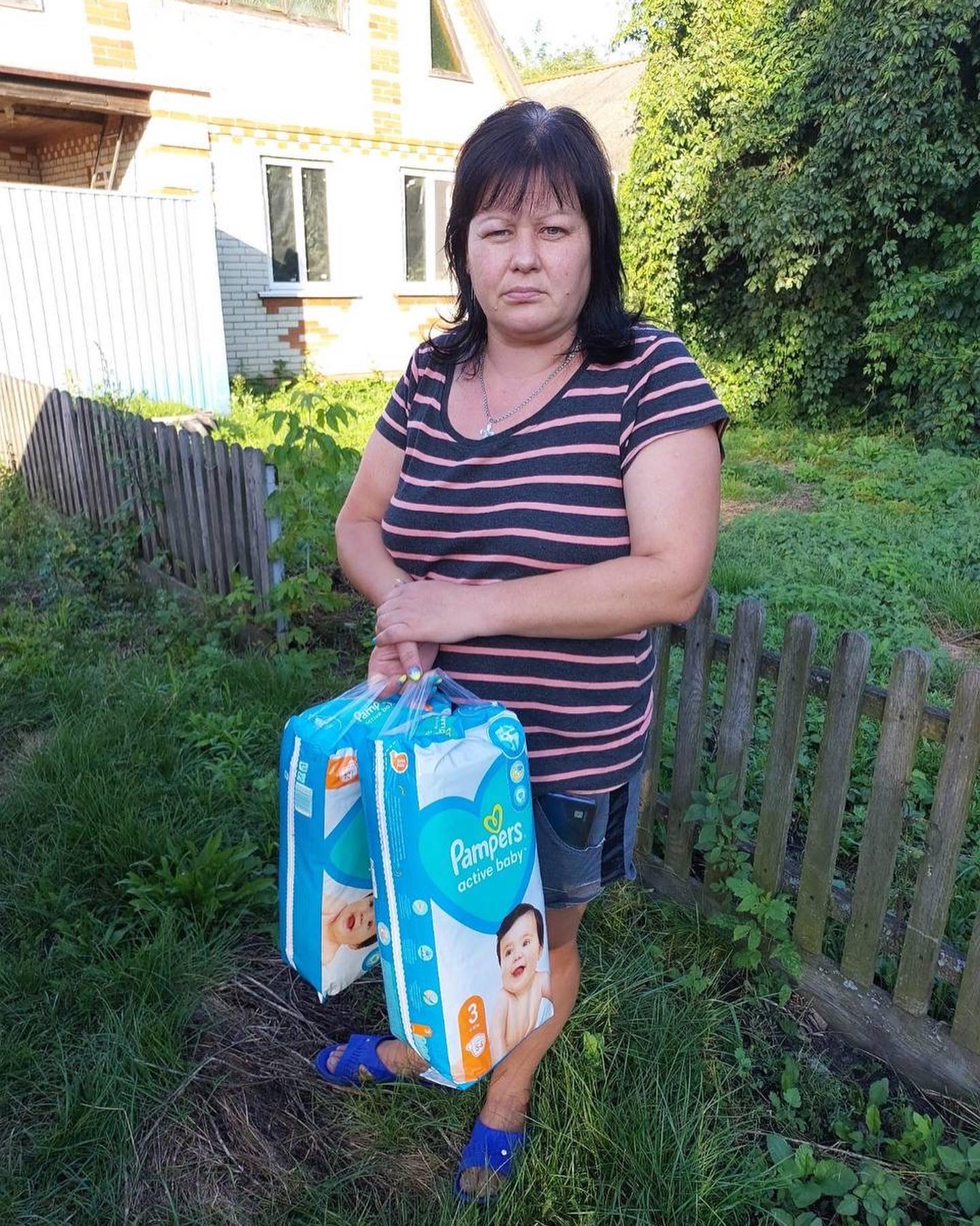 A woman holding two boxes of diapers in front of her house.