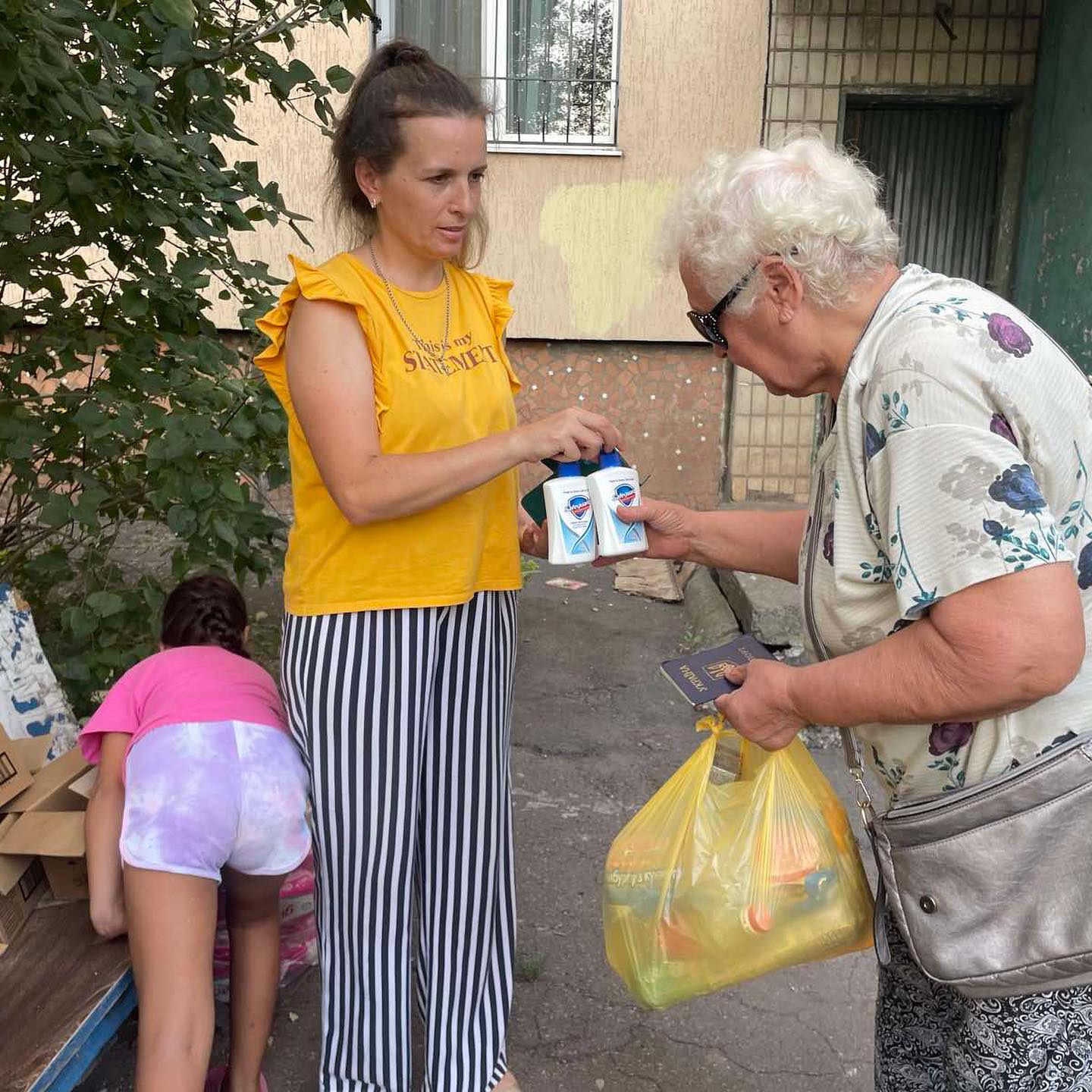 A woman handing a bag of food to a young girl.